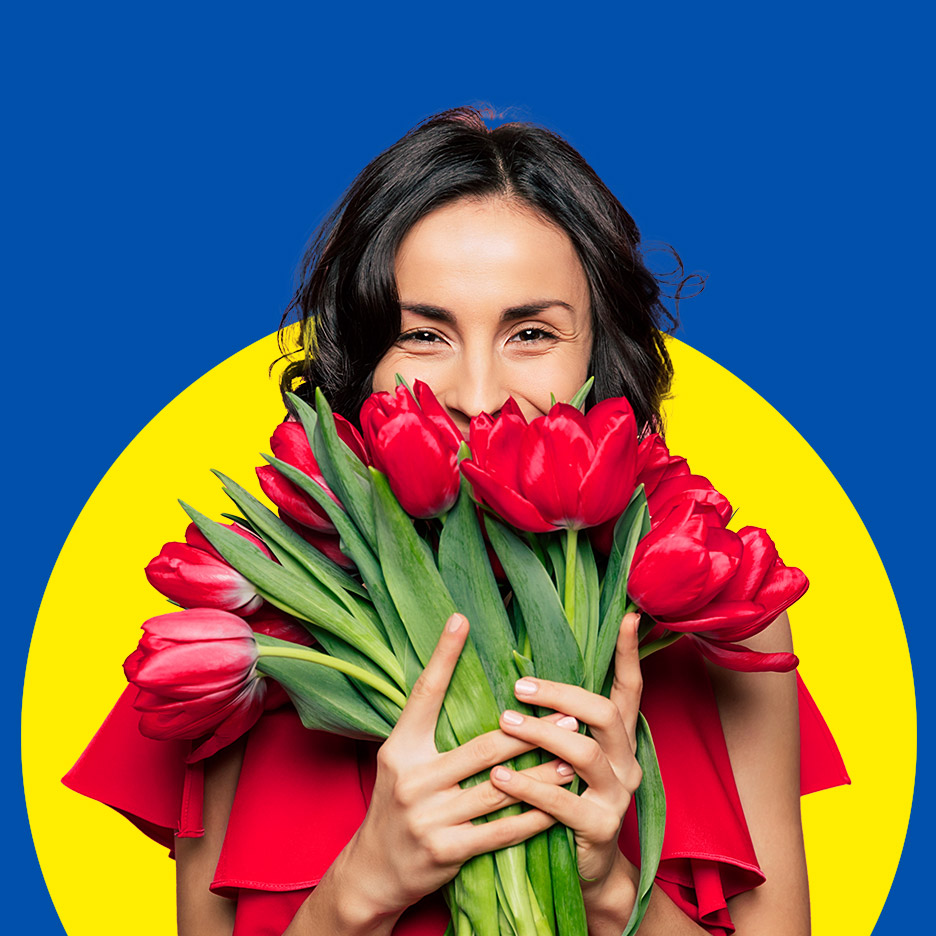 Vrolijke vrouw met een boeket rode tulpen voor een blauw-gele achtergrond.