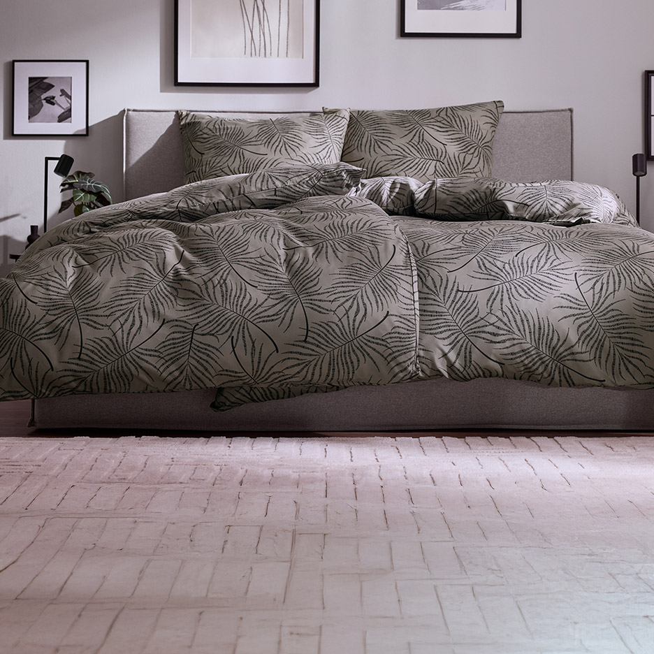 Bed met grijs beddengoed met bladprint en bijpassende kussens in een slaapkamer.