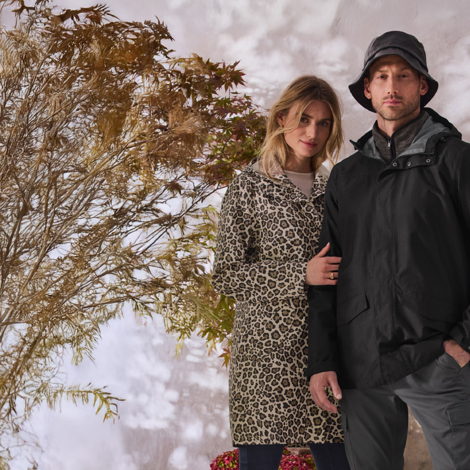 Man en vrouw in zwarte en luipaardprint regenjassen, staand bij een boom.