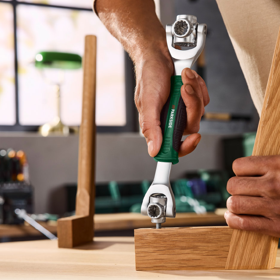 Handen die een Parkside moersleutel gebruiken om een bout in een houten plank te draaien.