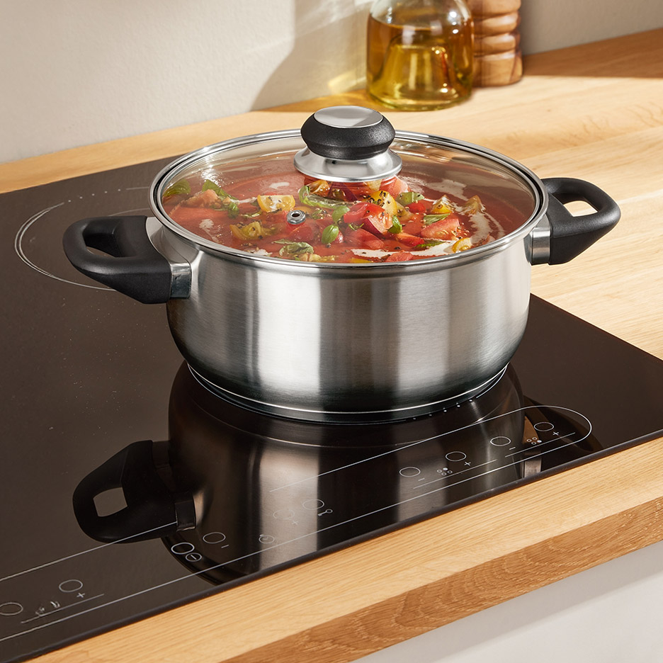 Roestvrijstalen kookpan met glazen deksel op een inductiekookplaat, gevuld met tomatensaus.