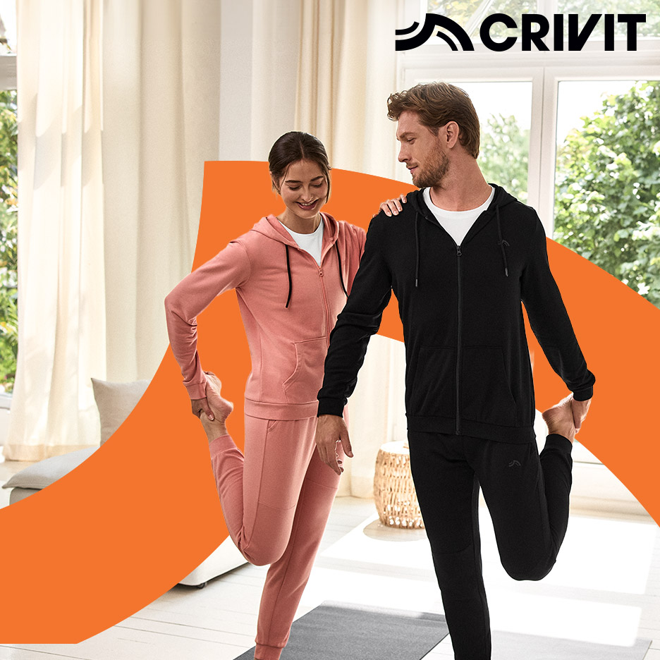 Man en vrouw in sportkleding rekken zich uit op een yogamat in een lichte kamer.