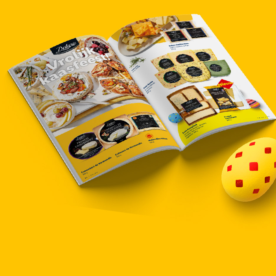 Een open magazine met een assortiment kazen, waaronder Franse camembert en romige kazen, en een gele paasdecoratie.