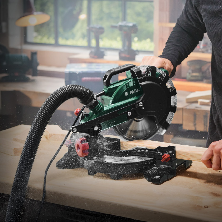 Een man gebruikt een afkortzaag om hout te zagen in een werkplaats.