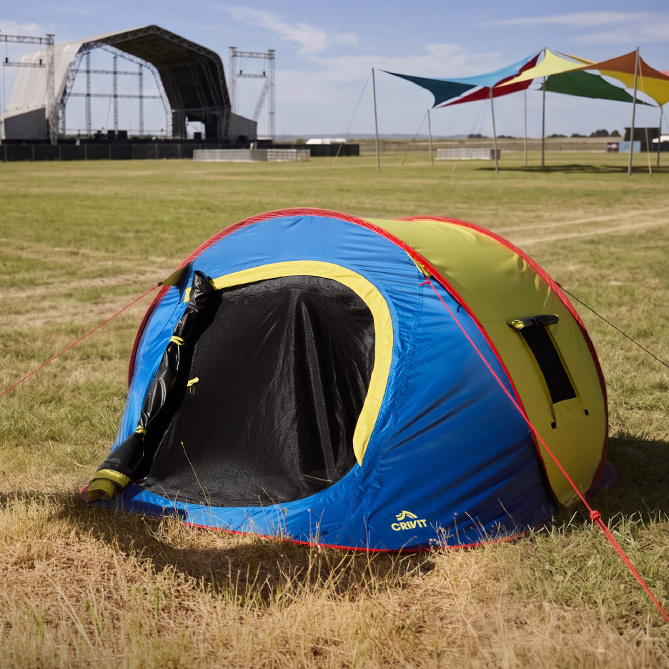 Blauwe en gele pop-up tent op een grasveld met een festivalpodium op de achtergrond.