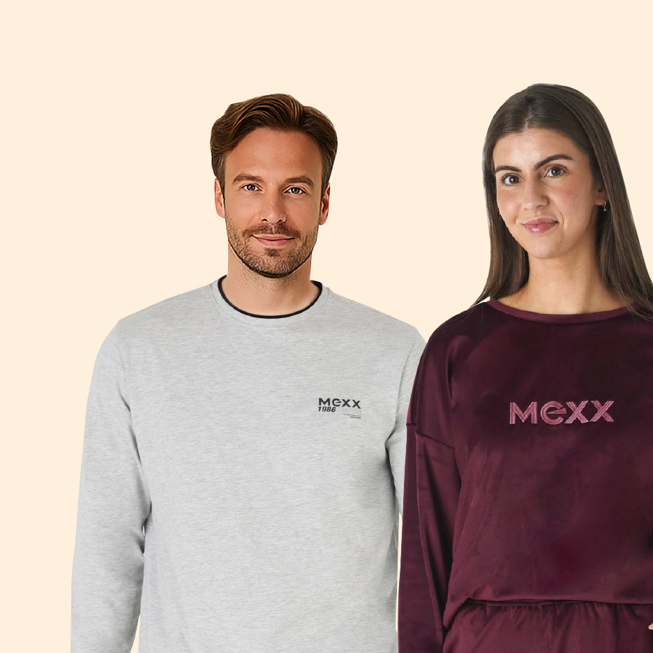 Vrouw in zwarte thermoshirt en legging, glimlachend en leunend tegen een muur.