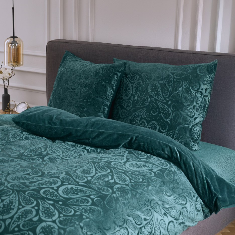 Donkergroen beddengoed met paisley-patroon op een bed.