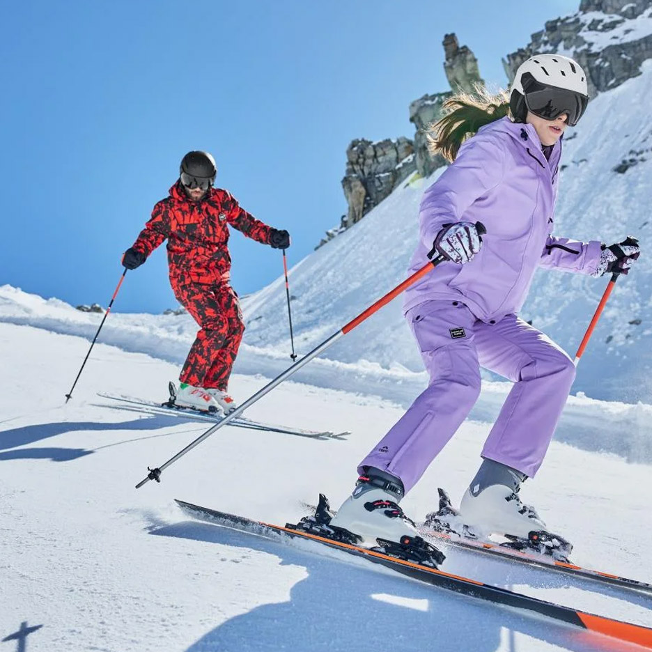 Twee skiërs in paarse en rode ski-outfits op een besneeuwde berghelling.