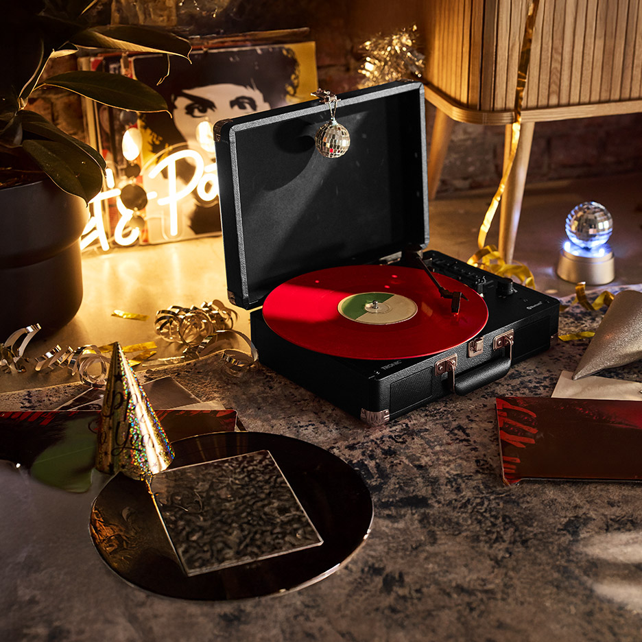 Draagbare platenspeler met rode vinylplaat, feestdecoraties en neonlicht.