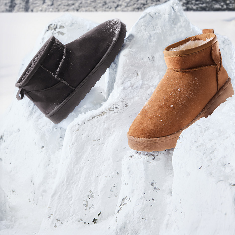 Twee warme winterlaarzen, één bruin en één zwart, staan in de sneeuw.