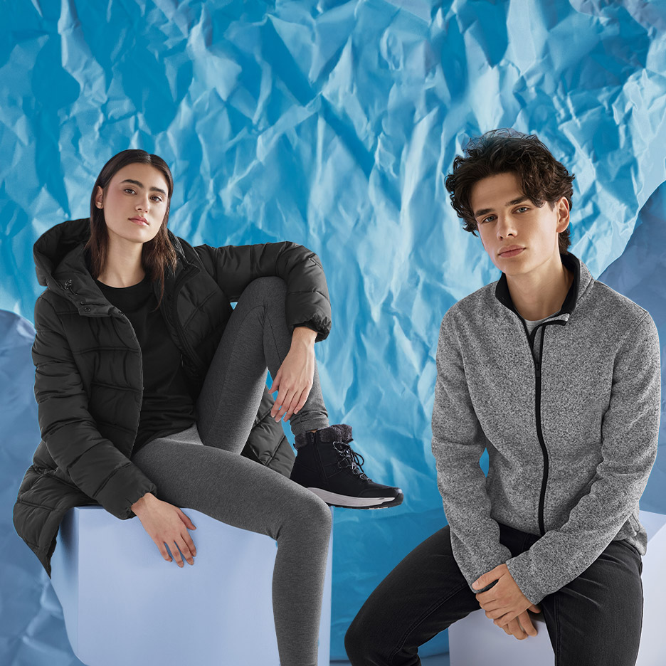 Vrouw in zwarte gewatteerde jas en grijze legging, man in grijs fleecejack en zwarte jeans.