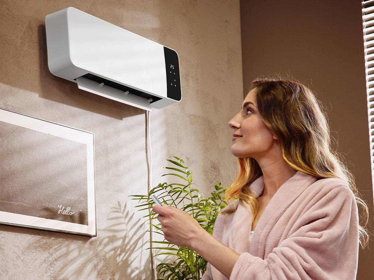 Vrouw in badjas stelt wandgemonteerde airconditioner in met afstandsbediening.