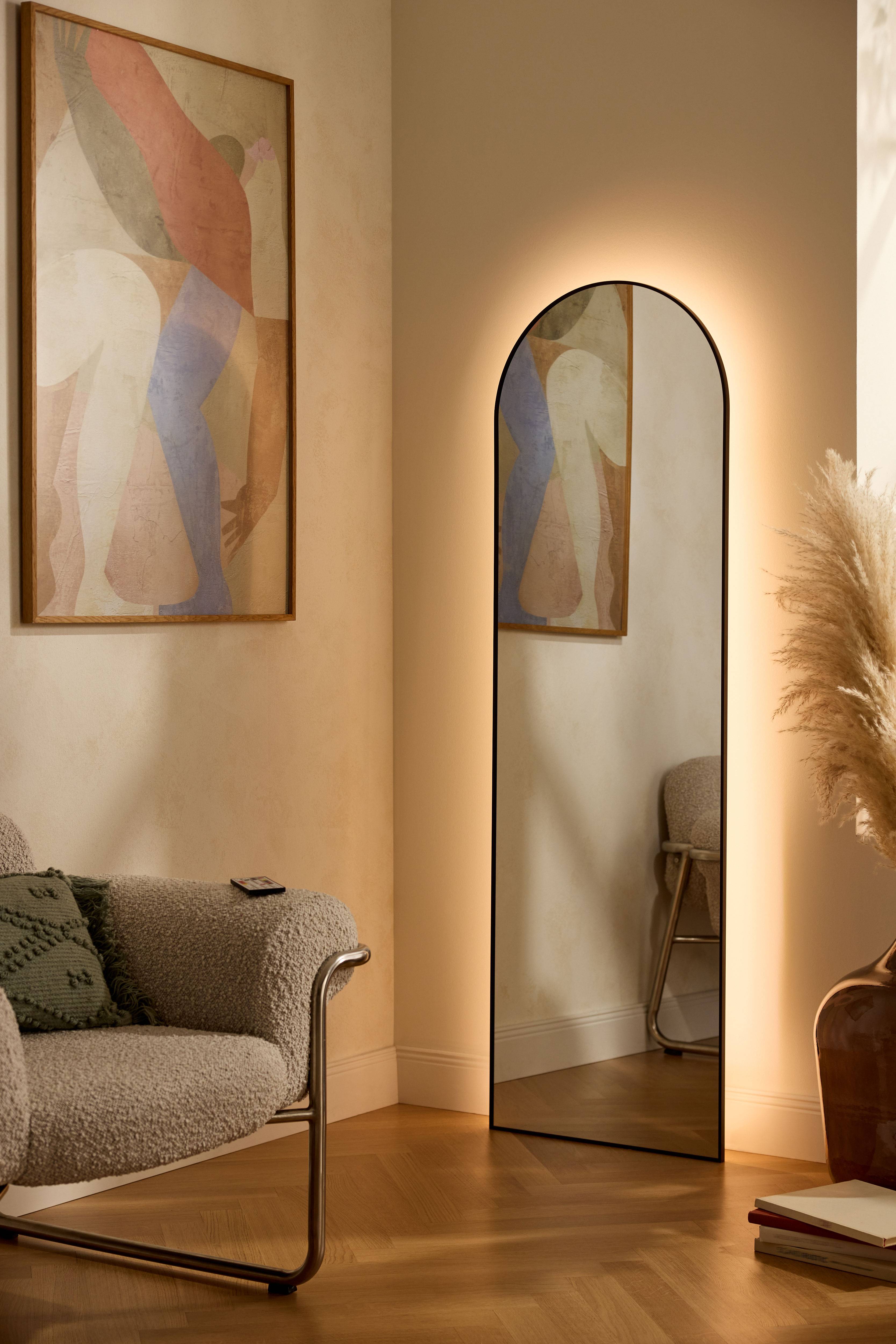 Verlichte spiegel en abstract schilderij in een moderne woonkamer met fauteuil en pampasgras.
