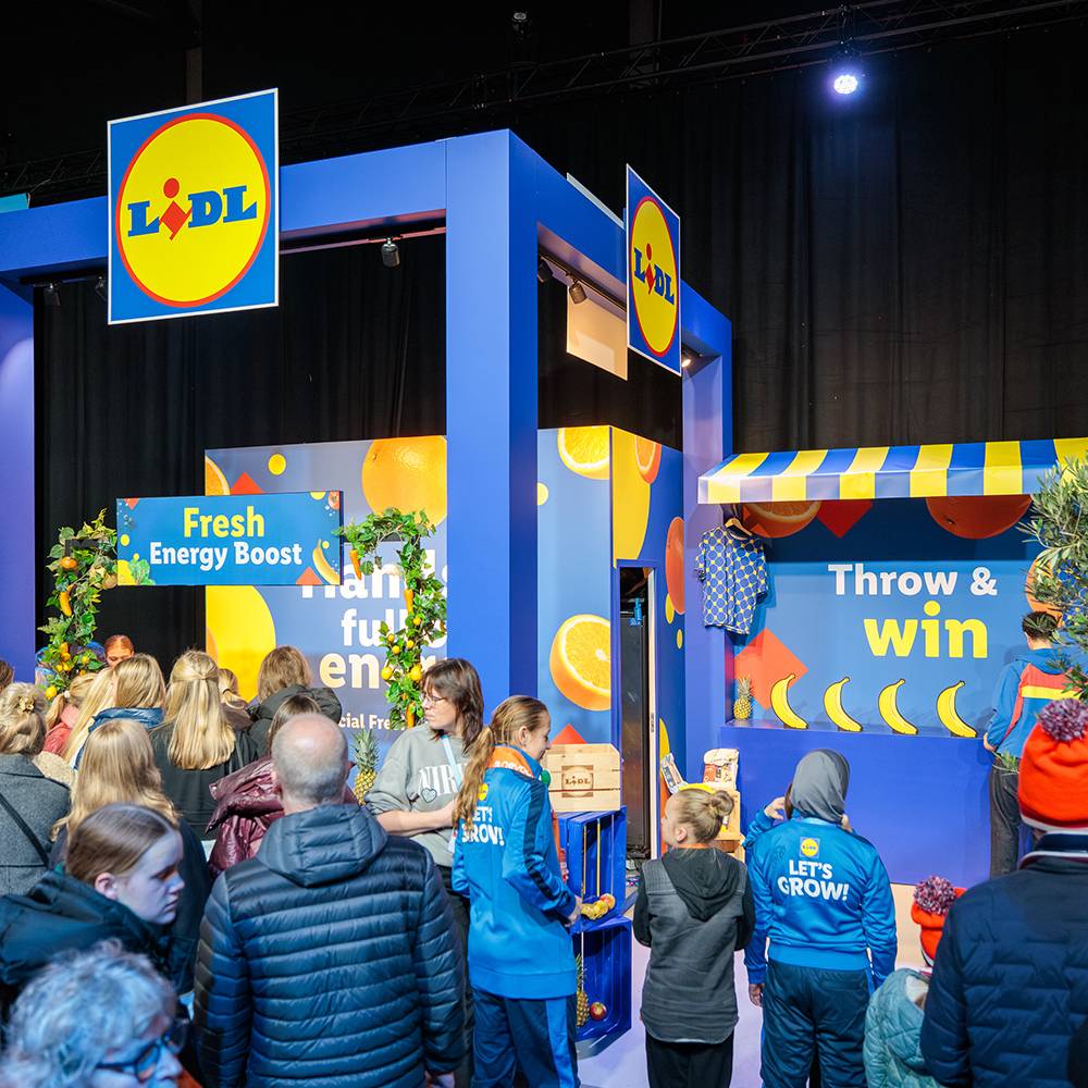 Mensen bij een Lidl-stand met fruit en de tekst 'Fresh Energy Boost' en 'Throw & win'.