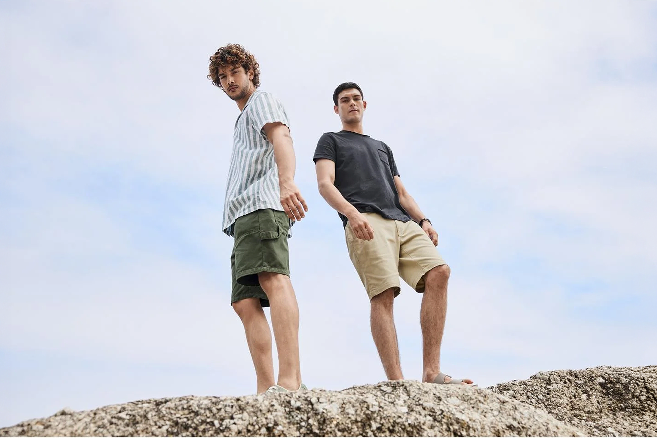 Twee mannen in casual shorts en T-shirts staan op een rots onder een bewolkte hemel.