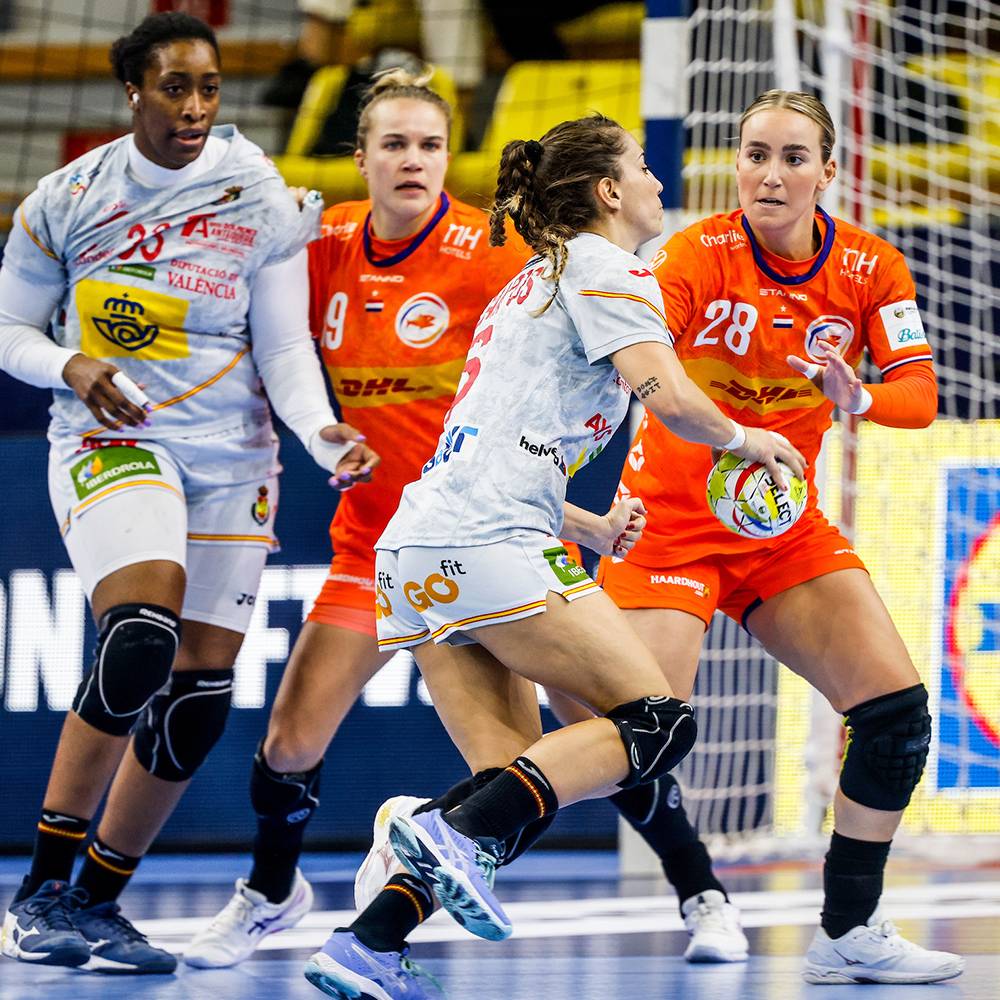 Vrouwenhandbalwedstrijd met spelers in oranje en witte tenues, met een bal.