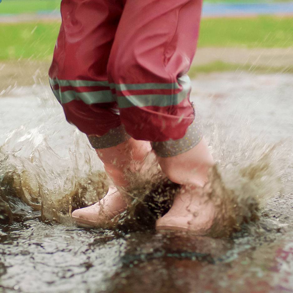 Kind in rode waterdichte broek en laarzen springt in een plas.