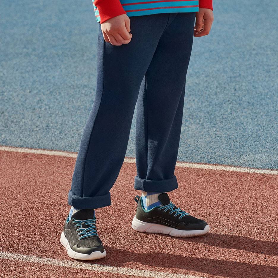 Donkerblauwe joggingbroek en zwarte sneakers met blauwe veters op een atletiekbaan.