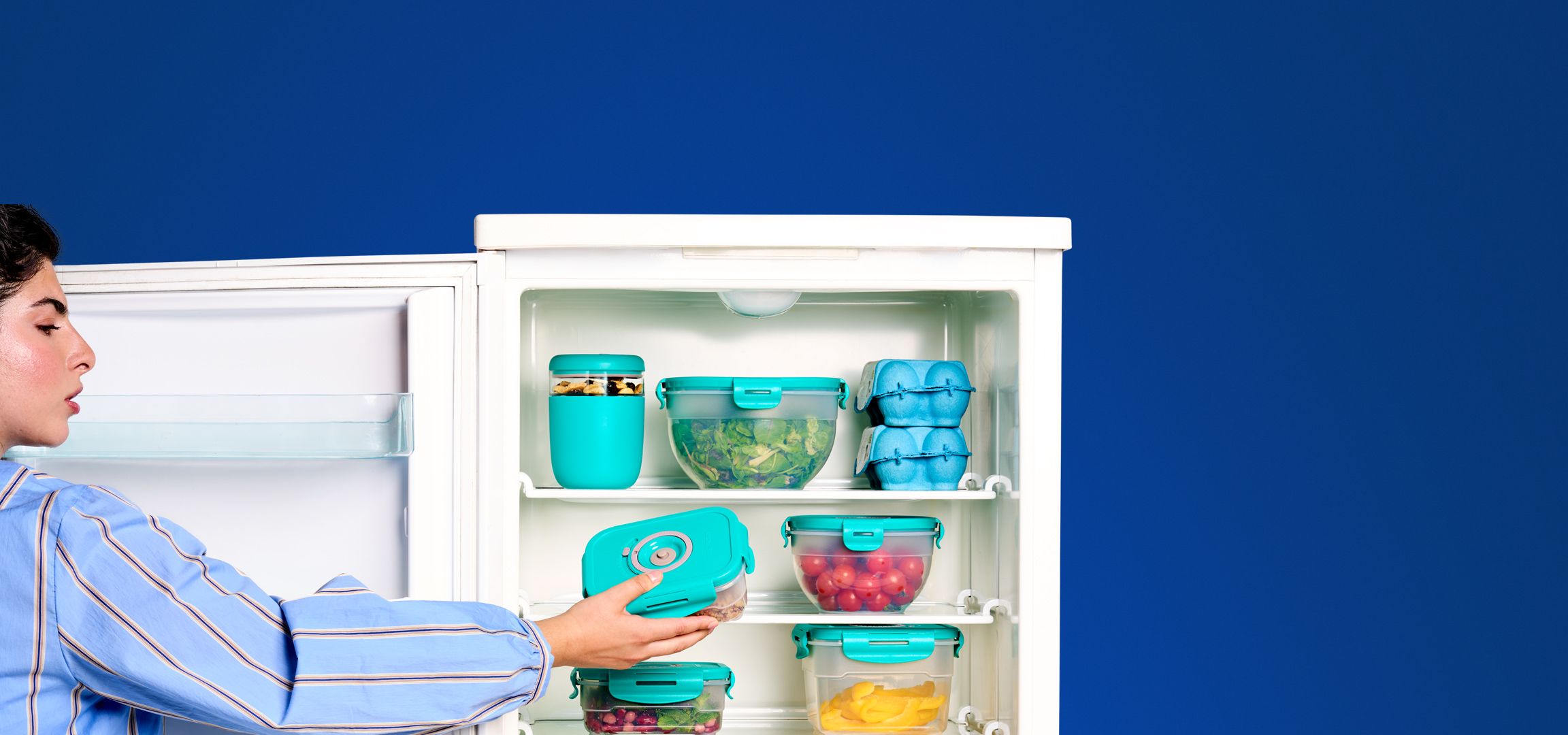 Vrouw pakt een vershouddoos met voedsel uit een koelkast vol met maaltijdprepcontainers.