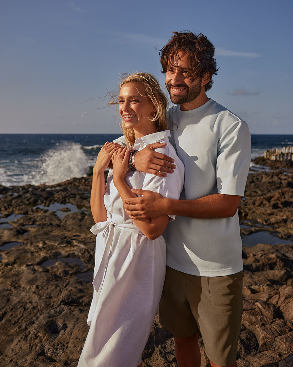 Paar op het strand, vrouw in witte jurk, man in lichtblauw T-shirt en korte broek.