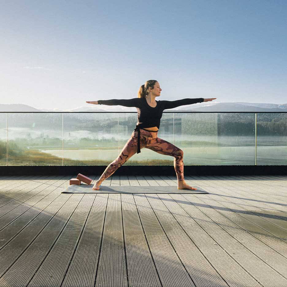 Vrouw in sportlegging en top doet yoga op een terras met uitzicht.