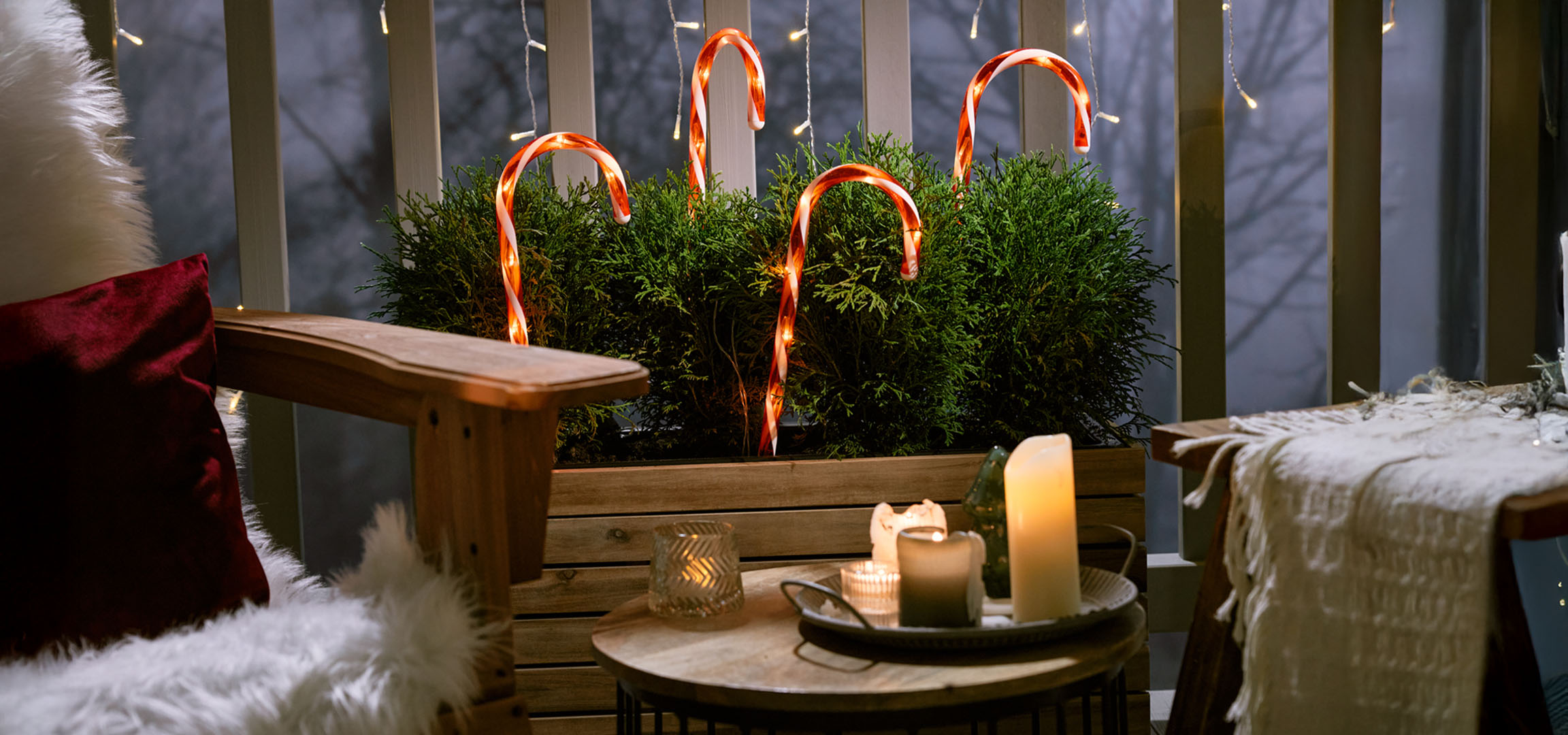 Kerstversierd balkon met een stoel, kaarsen en zuurstokken.