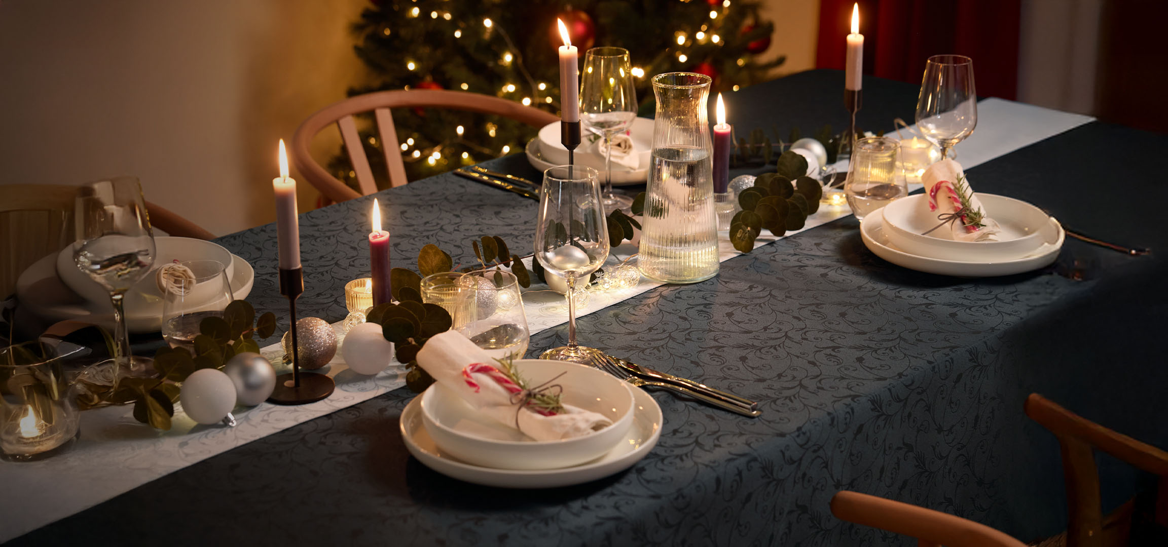Kersttafel met kaarsen, wit servies en feestelijke decoratie.