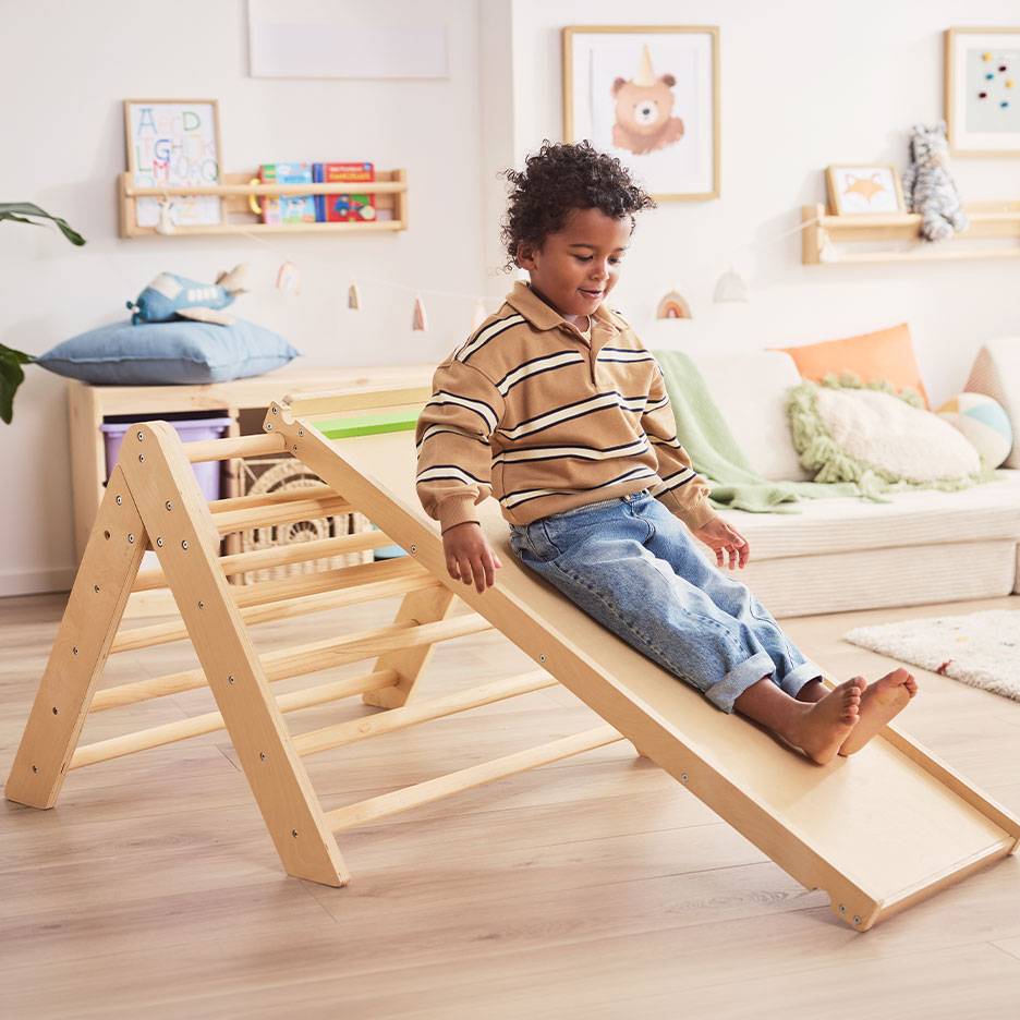 Kind speelt op een houten glijbaan en klimrek in een kinderkamer.