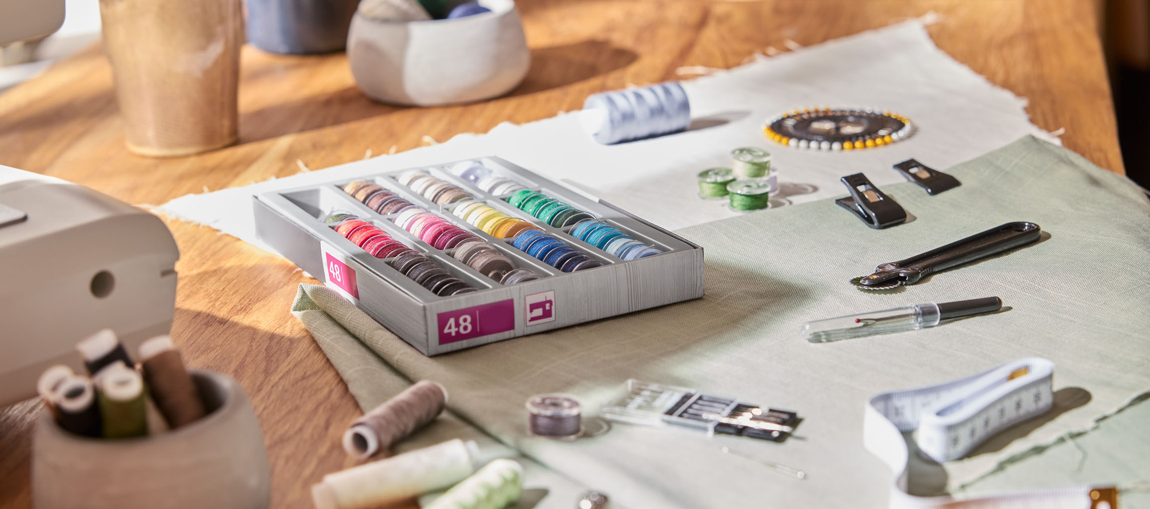 Naaibenodigdheden op een houten tafel, inclusief een draadorganizer met 48 spoelen, stof en diverse gereedschappen.