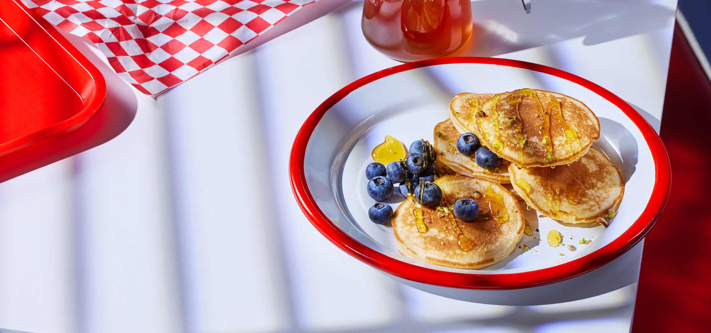 Een bord met pannenkoeken, bosbessen, honing en pistachenoten.