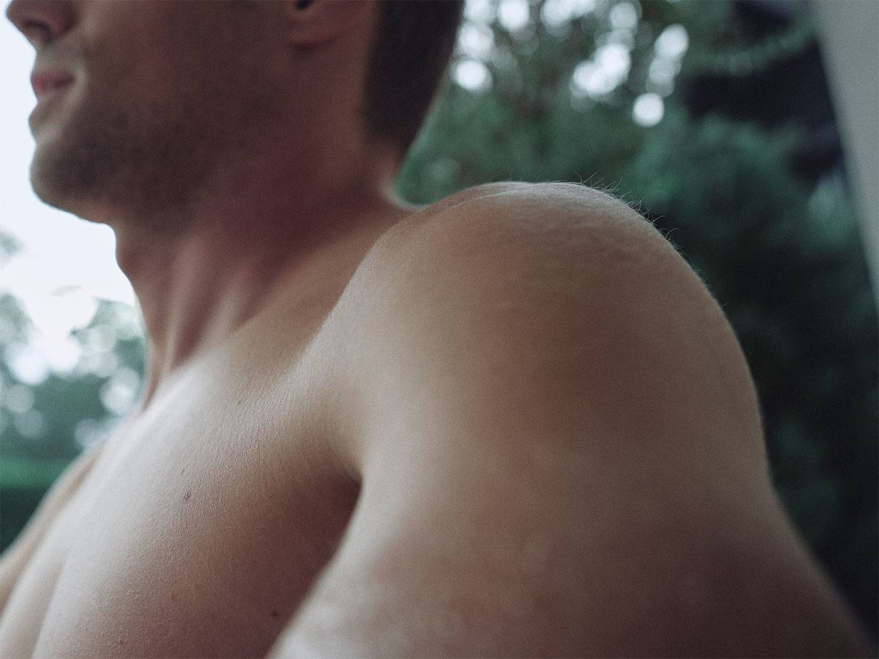 Close-up van een mannen schouder en nek, met een wazige groene achtergrond.