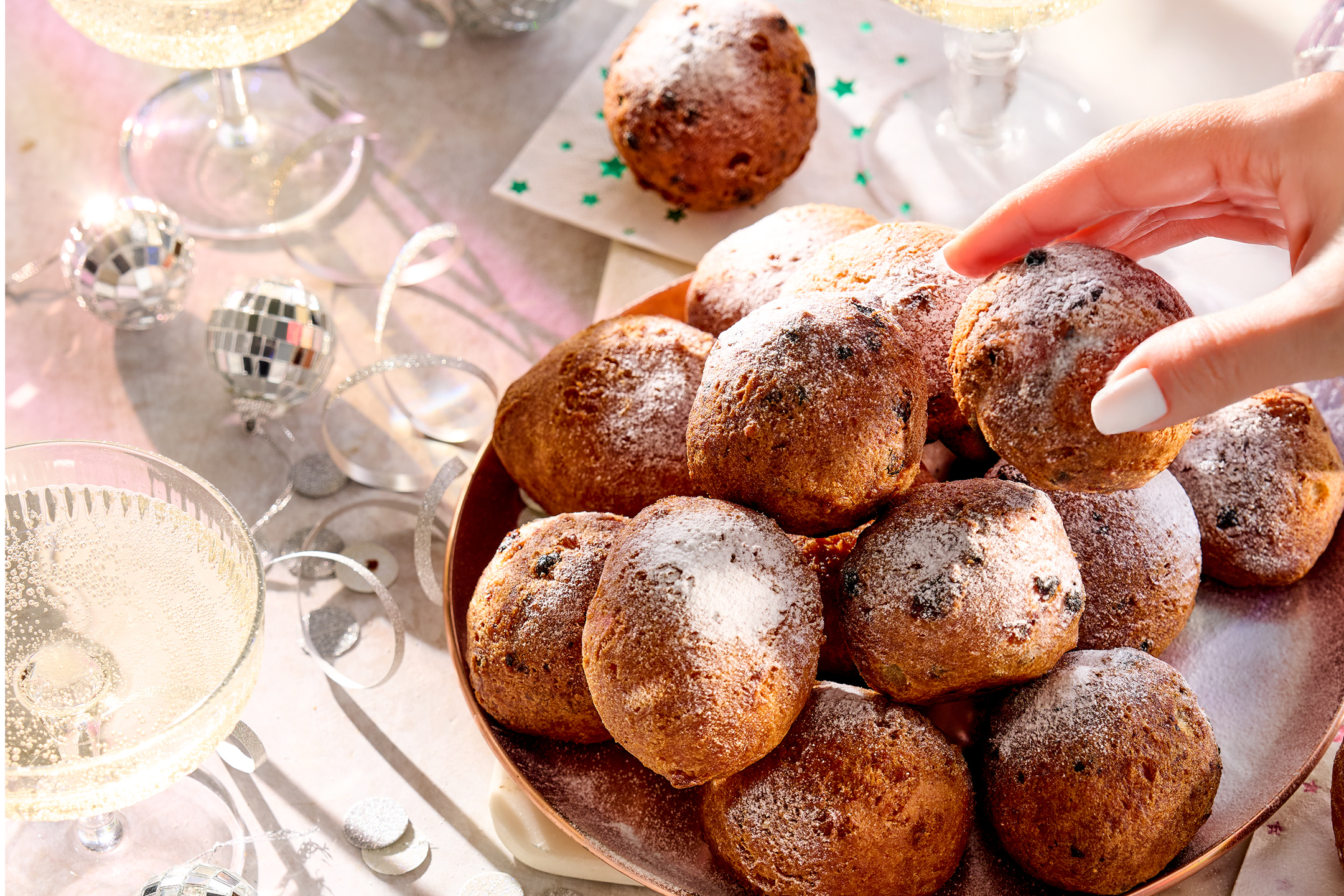 Oliebollen met poedersuiker op een schaal, met champagneglazen en feestelijke decoratie.
