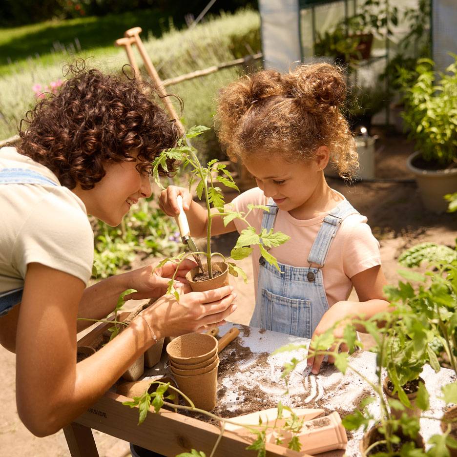 Moeder en kind planten zaailingen in biologisch afbreekbare potten, omringd door tuingereedschap.