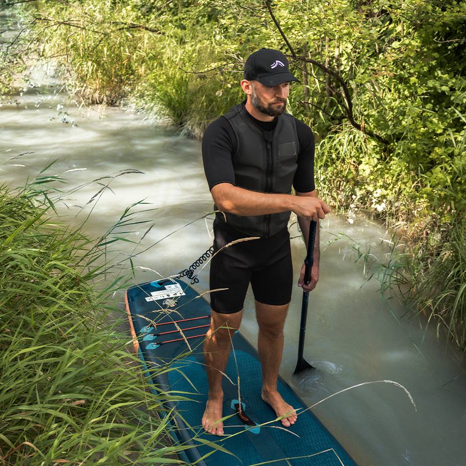 Man op een SUP-board in een rivier, draagt een wetsuit en zwemvest.