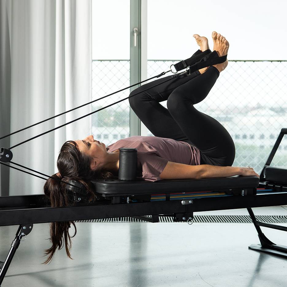 Vrouw traint benen op een Pilates reformer met weerstandsbanden.