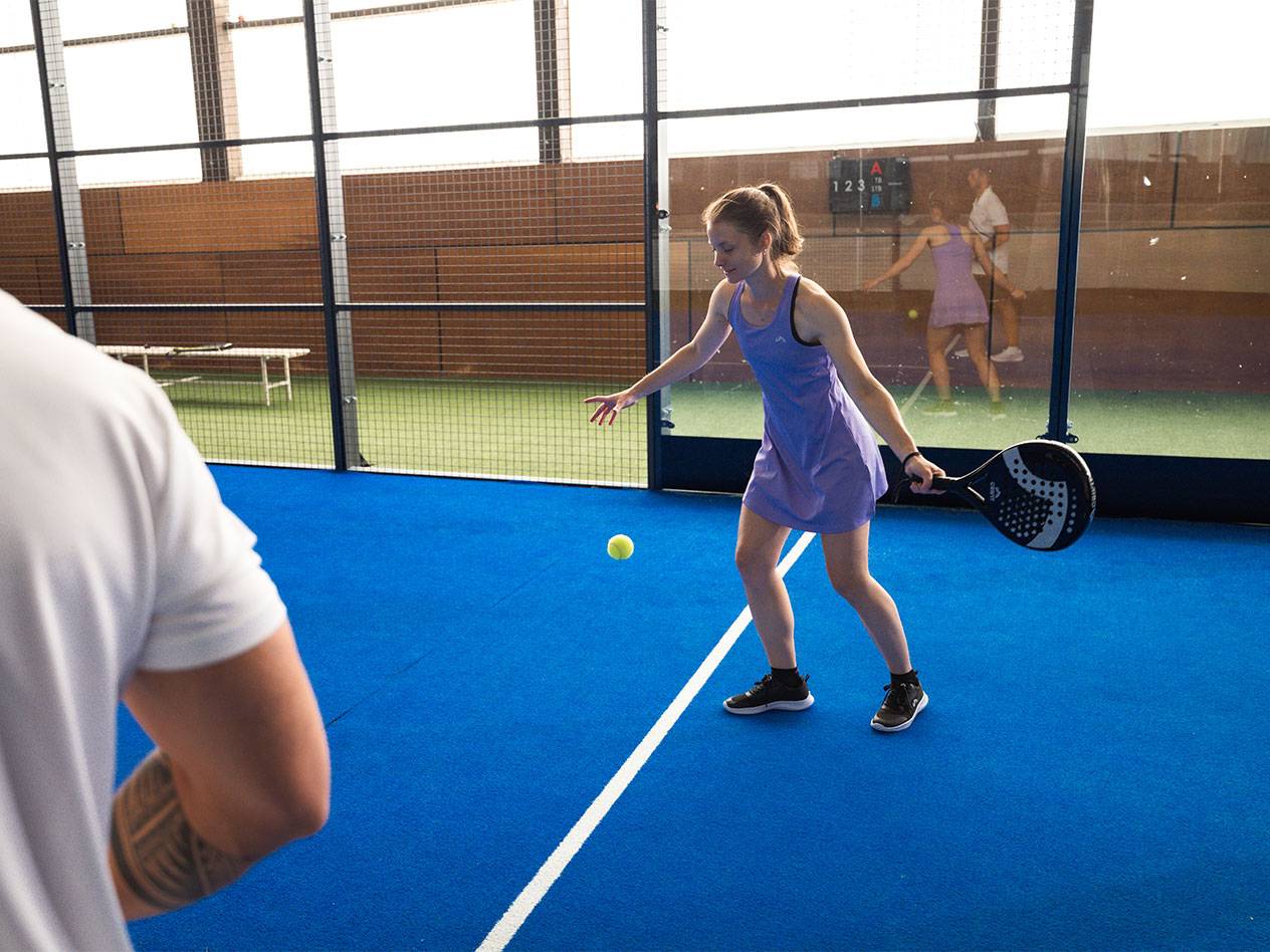 Vrouw in paarse sportjurk speelt padel met racket en bal.