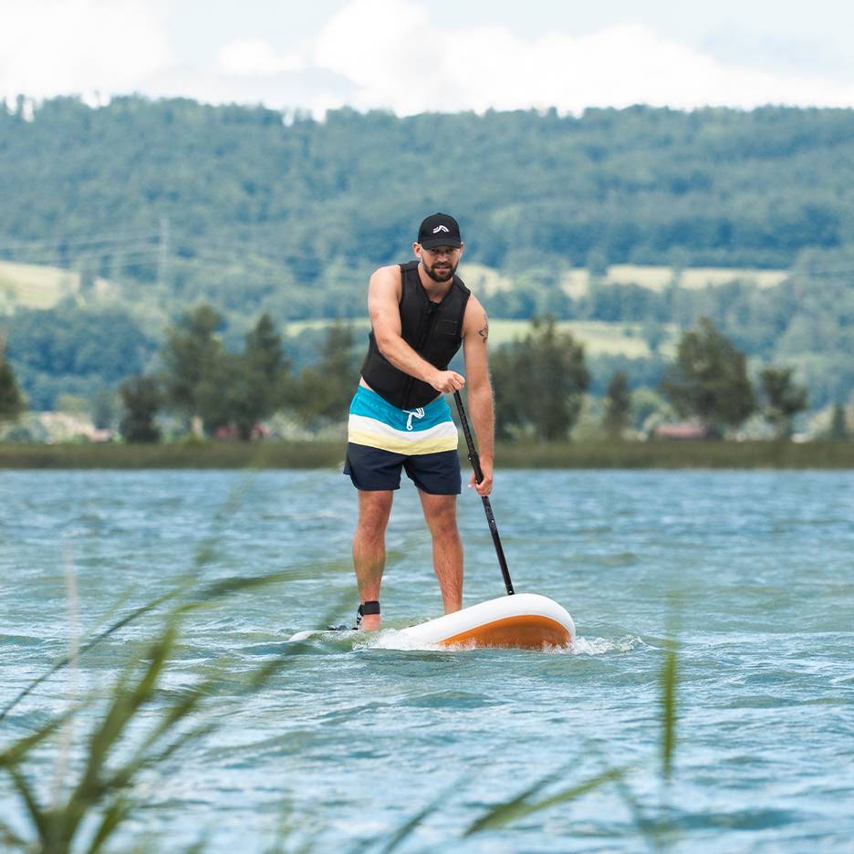 Man stand-up paddleboardend op een meer, met zwemvest en zwemshorts.