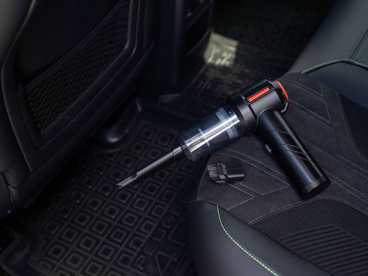 Compacte handstofzuiger met accessoires op een autostoel.