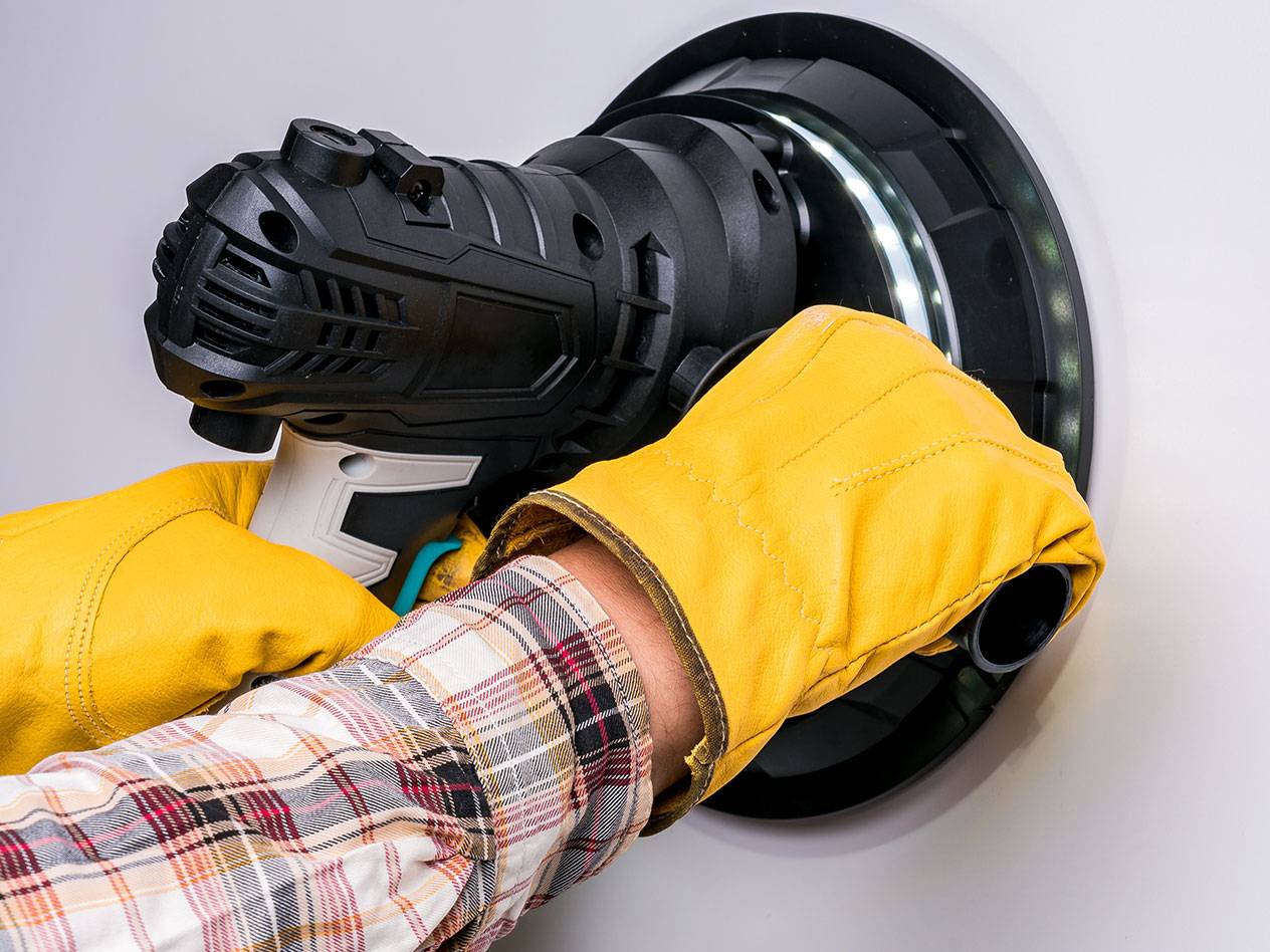 Elektrische wandschuurmachine met LED-licht, gebruikt door een persoon met handschoenen.