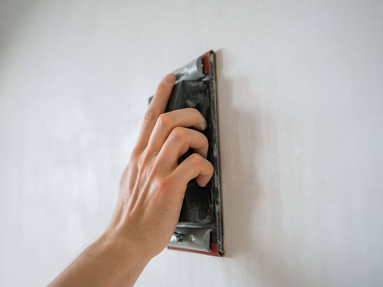 Handmatig schuren van een muur met een schuurblok