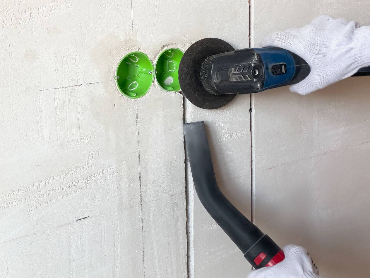 Elektrisch gereedschap snijdt groeven in een muur met een stofzuiger voor stof.
