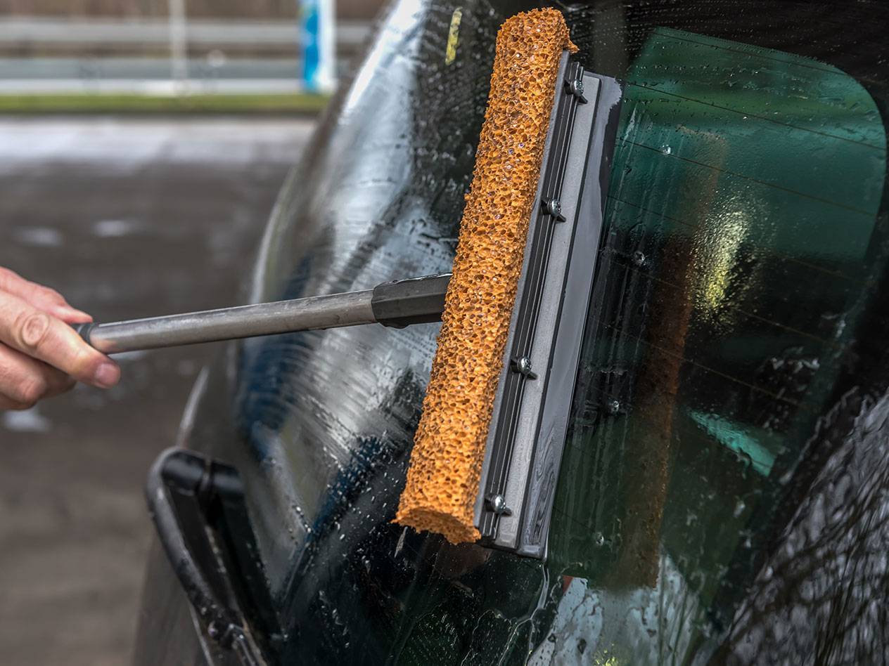 Ruitenreiniger met lange steel reinigt de achterruit van een auto.
