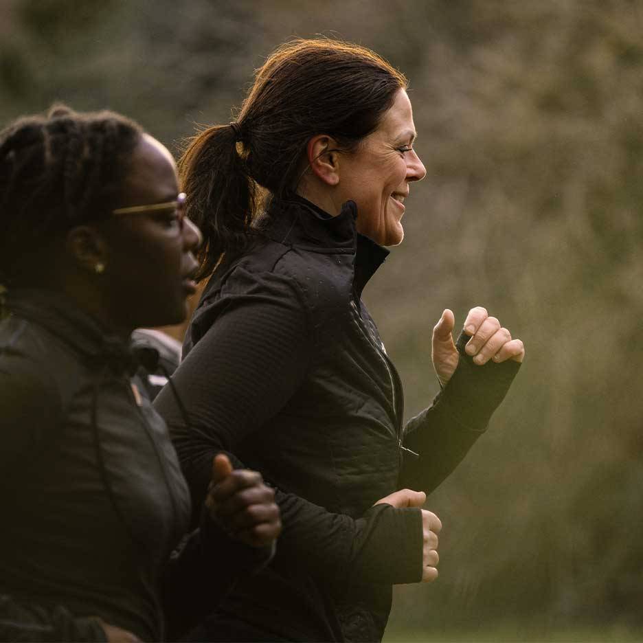 Twee vrouwen in sportkleding rennen buiten, één glimlachend.