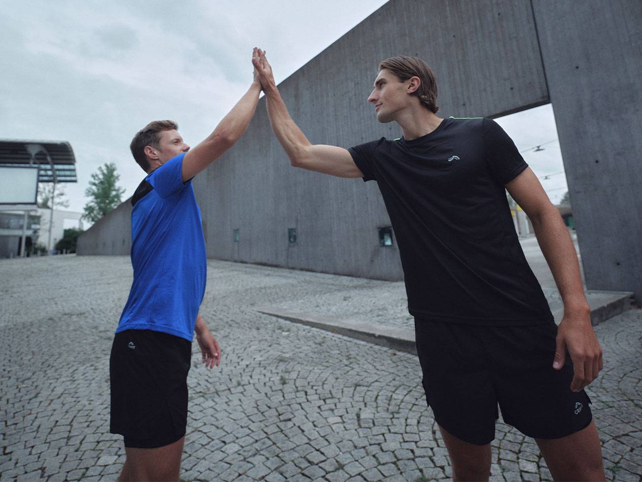Twee mannen in zwarte en blauwe sportshirts en shorts geven een high five.