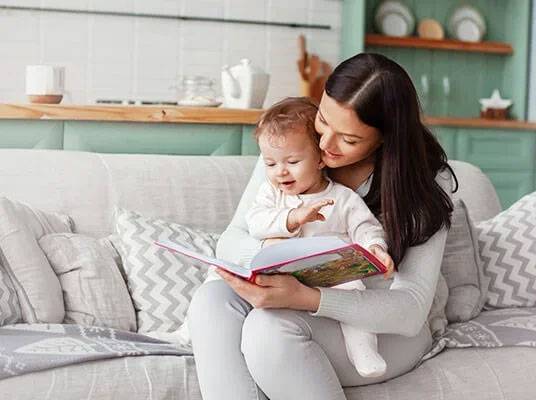 Moeder leest een boek voor aan haar kind op de bank.