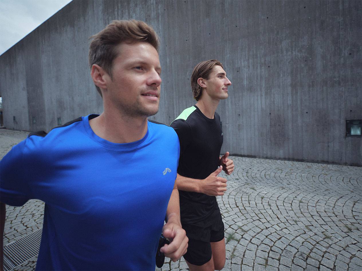 Twee mannen rennen in sportieve T-shirts en shorts, één blauw en één zwart.