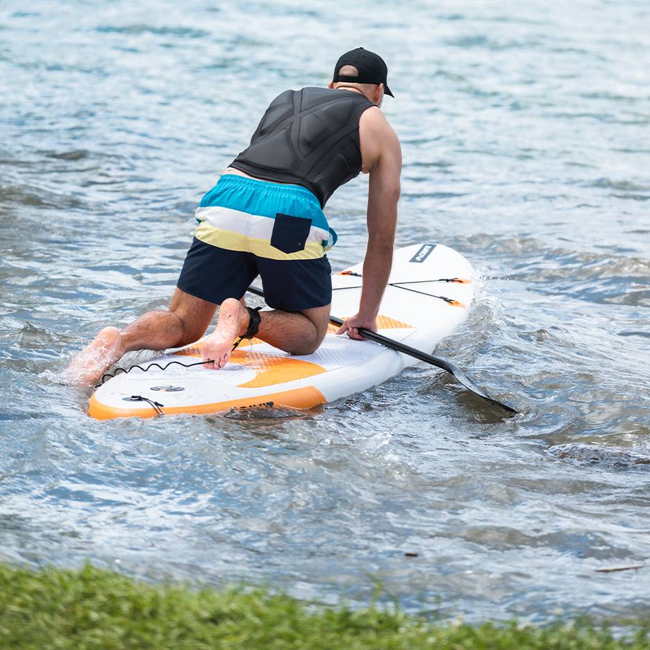 Man knielend op een paddleboard met peddel in het water.