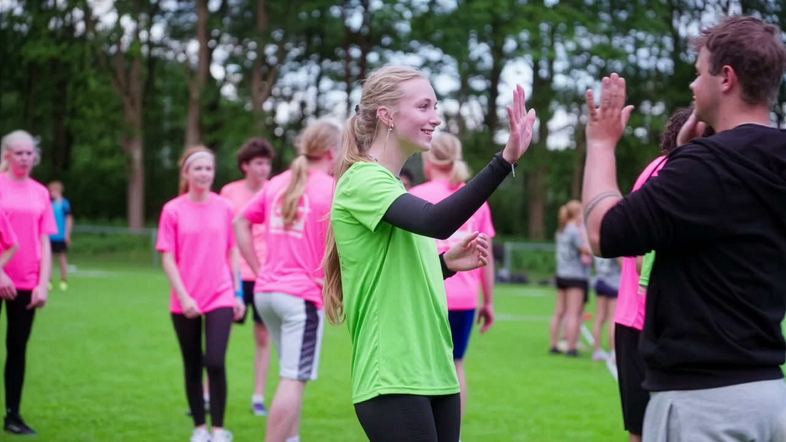 Jonge mensen in sportkleding geven elkaar een high five op een grasveld.