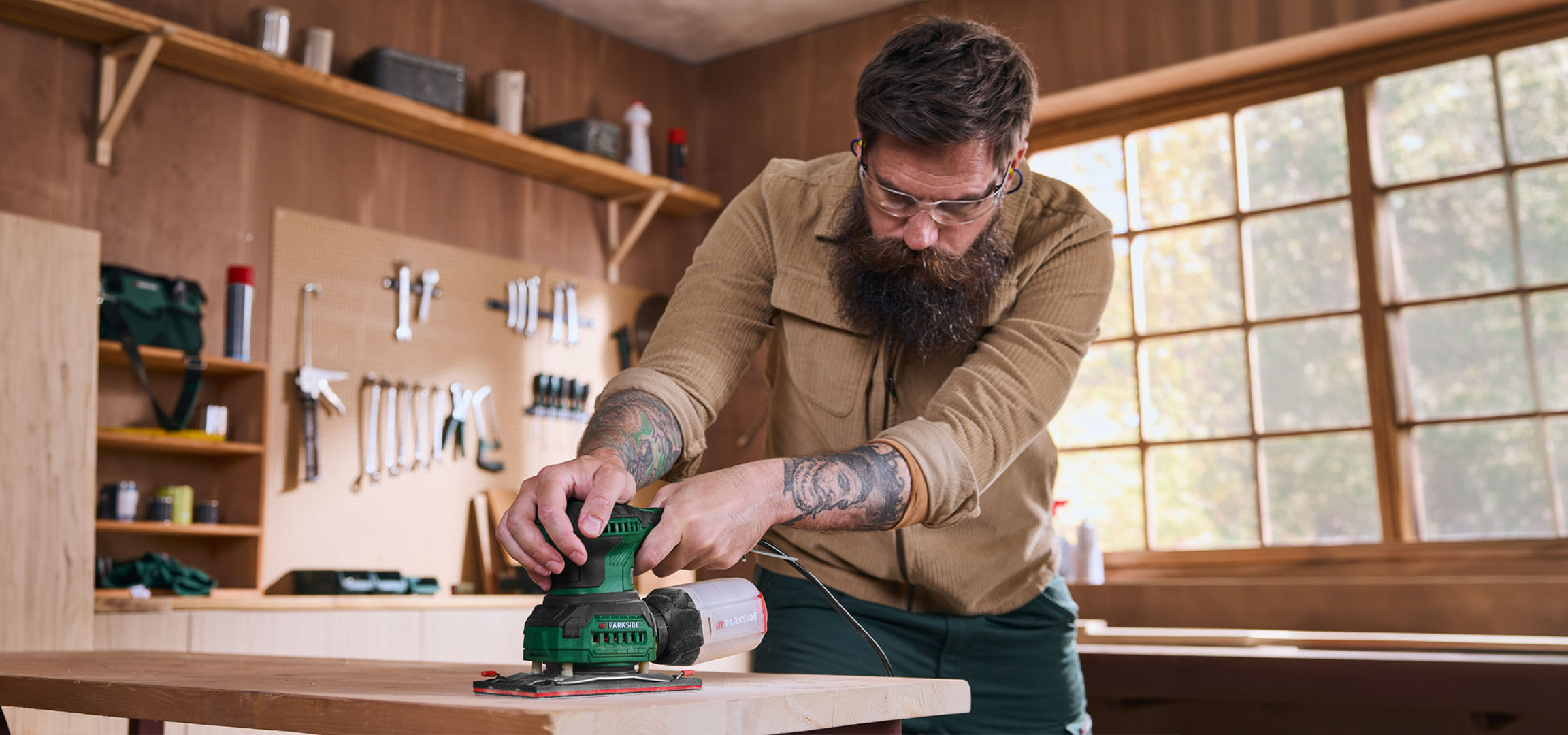 Man schuurt een houten plank met een elektrische schuurmachine in een werkplaats.