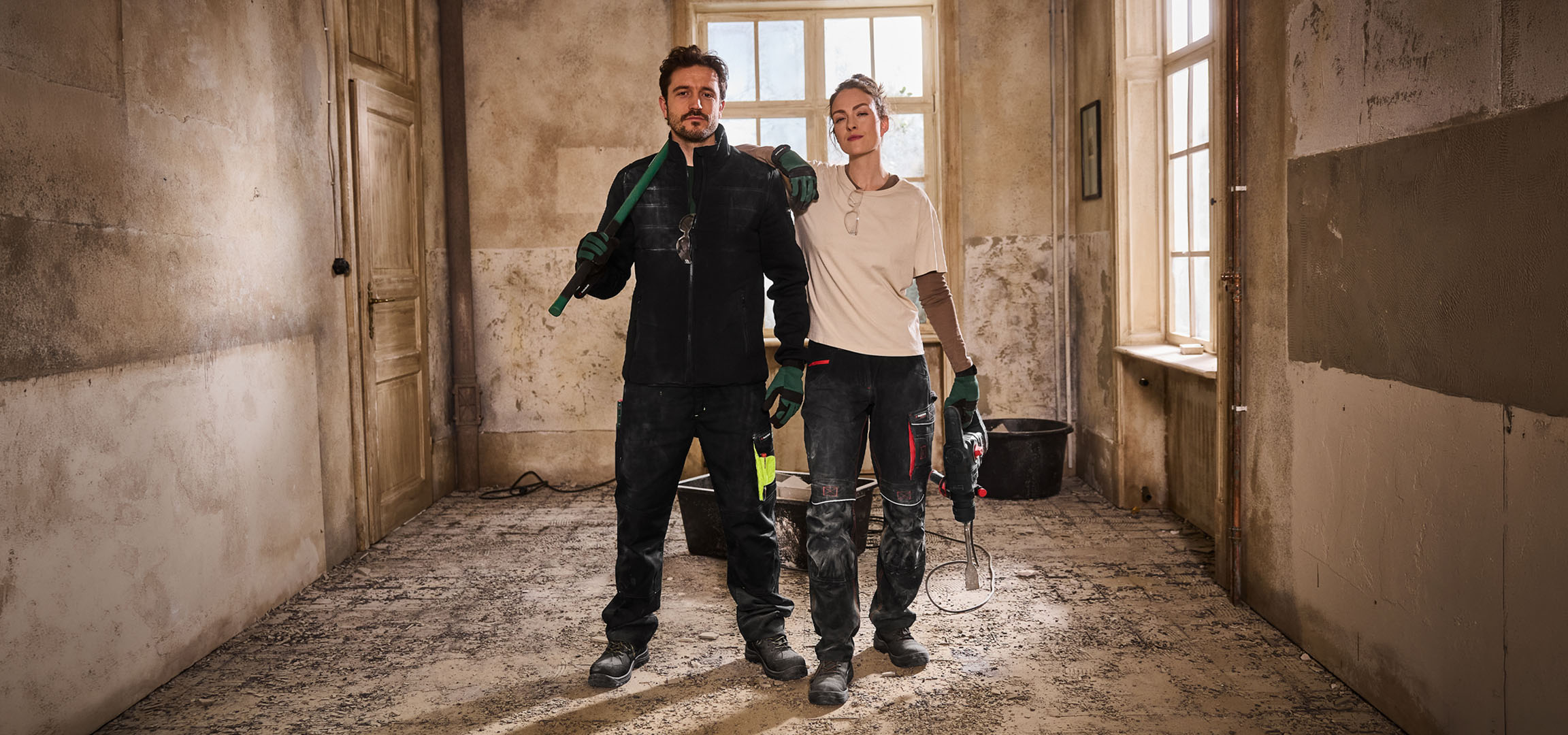 Twee bouwvakkers in werkkleding met gereedschap op een bouwplaats.